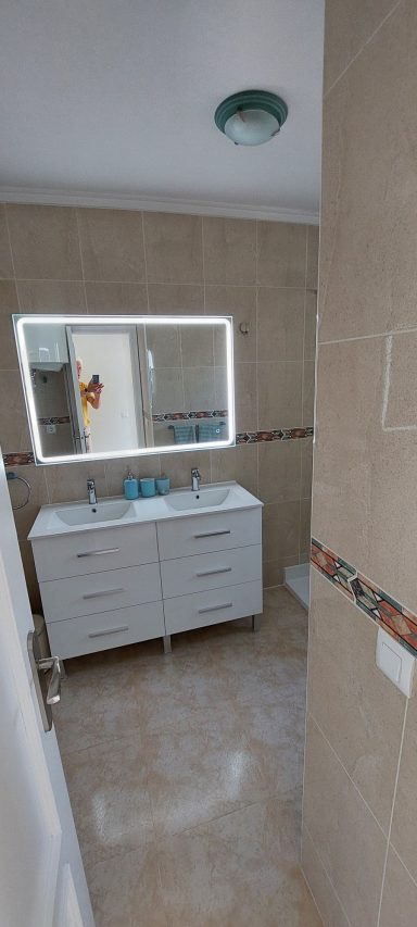 Badkamer Moderne badkamer met witte wastafel en grote spiegel, lichte tegels en neutralen kleuren.