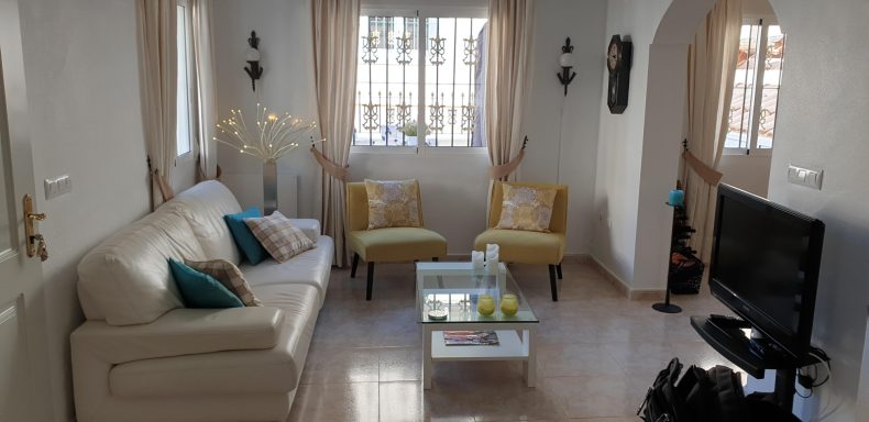 Huiskamer Een lichte woonkamer met een bank, twee gele stoelen en een tv. Decor met planten.